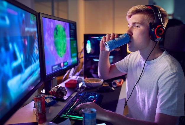 Foto adolescente bebendo cafeína e energético jogando em casa usando duas telas de computador à noite