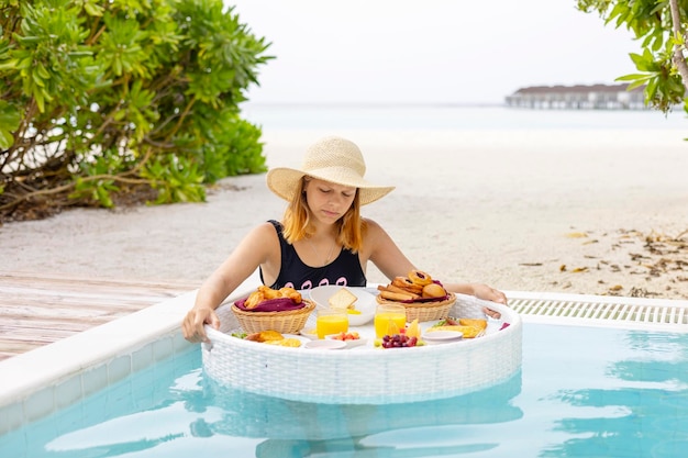 Foto adolescente bonita com servida bandeja flutuante na piscina com bebidas e lanches em resort de ilha tropical nas maldivas