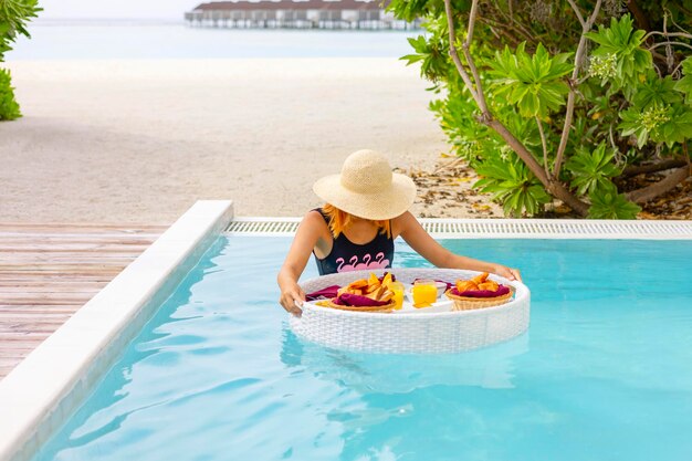 Foto adolescente bonita com servida bandeja flutuante na piscina com bebidas e lanches em resort de ilha tropical nas maldivas