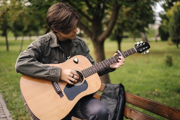 Adolescente bonito tocando violão com o capo rapaz sentado no banco e tocando música
