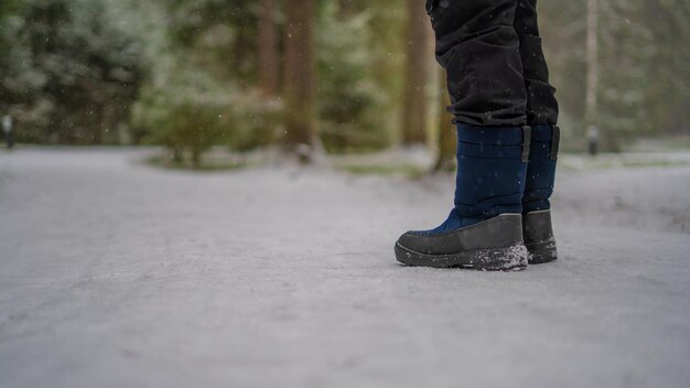 Un adolescente con botas azules de invierno se para sobre la nieve blanca en un camino halagador.