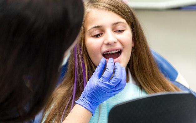 Foto adolescente con brackets siendo examinado por el dentista con guantes en la clínica