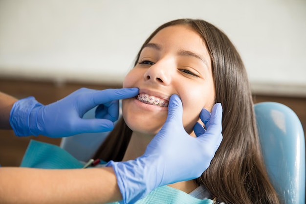 Foto adolescente con brackets siendo examinado por el dentista con guantes en la clínica