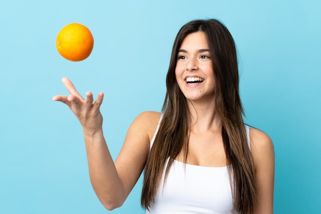 Adolescente brasileña sobre pared azul aislado sosteniendo una naranja