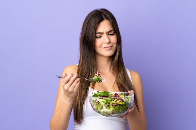 Adolescente brasileña sosteniendo una ensalada sobre pared púrpura aislado