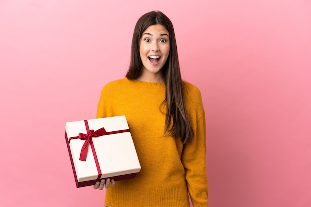 Adolescente brasileña sosteniendo un regalo sobre fondo rosa aislado con expresión facial sorpresa