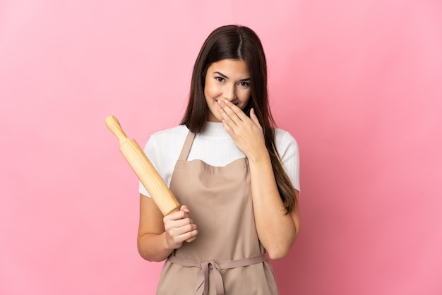 Adolescente brasileña sosteniendo un rodillo aislado en la pared rosa feliz y sonriente cubriendo la boca con la mano