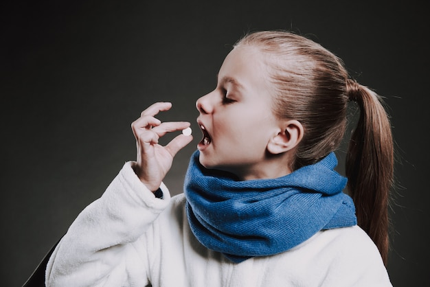 Adolescente en bufanda tejida pone la píldora en la boca.