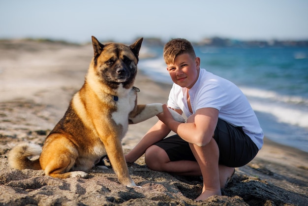 Adolescente con cabello rubio y correa en las manos juega y camina con un perro de raza Akina Inu en una playa salvaje a lo largo del Mar Negro