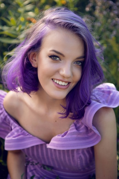 Foto adolescente con cabello teñido de púrpura y un piercing en la nariz en la hierba con un ramo de flores y un vestido corto