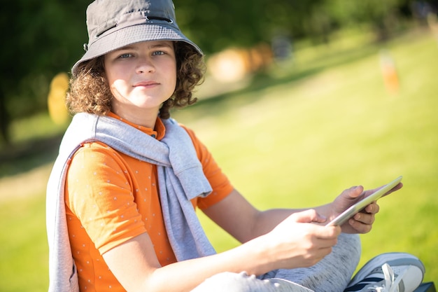 Adolescente calmo com seu gadget sentado ao ar livre