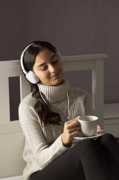 Foto adolescente en la cama escuchando música con auriculares y taza de té