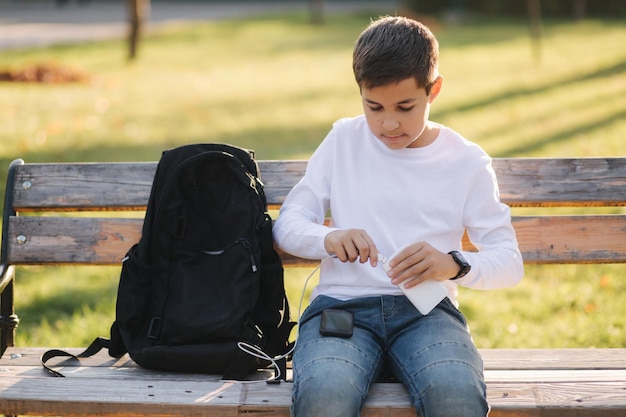 Adolescente con camisa blanca usa un banco de energía para cargar su teléfono inteligente en el exterior Batería baja en el teléfono inteligente