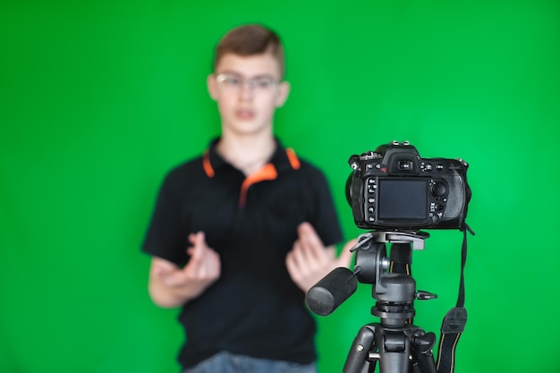 Foto un adolescente con una camiseta negra de fondo verde graba un video para un blog usando una cámara y un