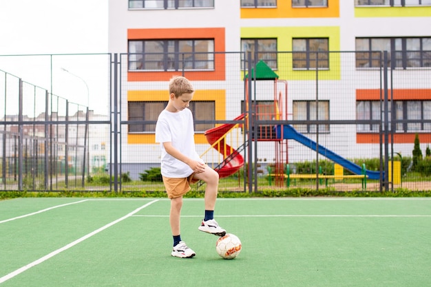 Un adolescente se para en un campo verde en el patio de la escuela con una pelota de fútbol en entrenamiento