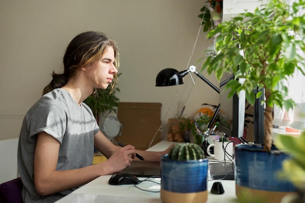 Un adolescente en casa trabajando en una computadora usando una tableta gráfica para trabajar con imágenes