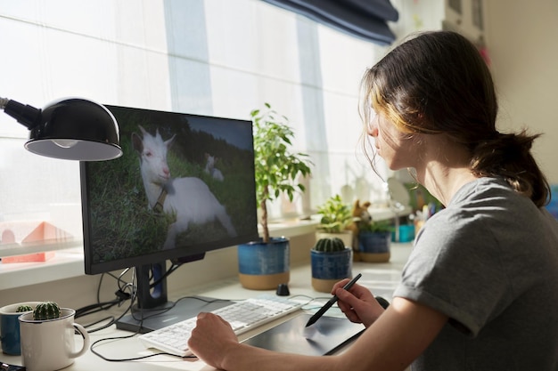 Un adolescente en casa trabajando en una computadora usando una tableta gráfica para trabajar con imágenes