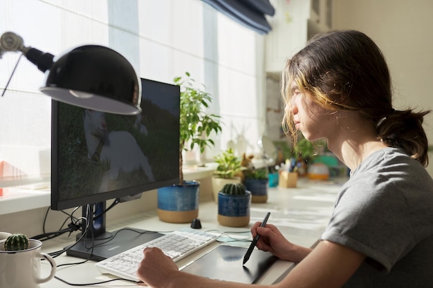 Un adolescente en casa trabajando en una computadora usando una tableta gráfica para trabajar con imágenes