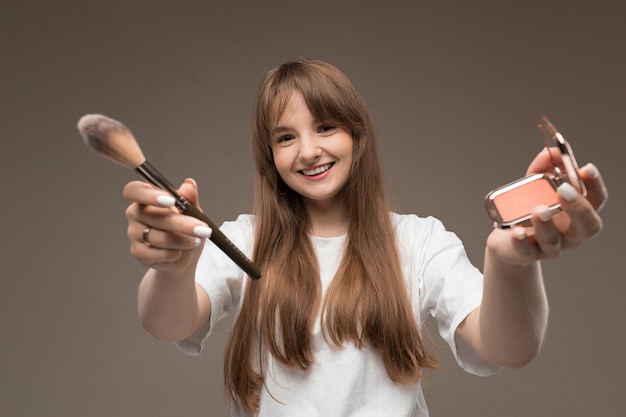 Foto adolescente caucasiano fazer maquiagem com pincéis isolados na parede marrom