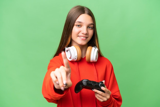 Una adolescente caucásica jugando con un controlador de videojuegos sobre un fondo aislado mostrando y levantando un dedo