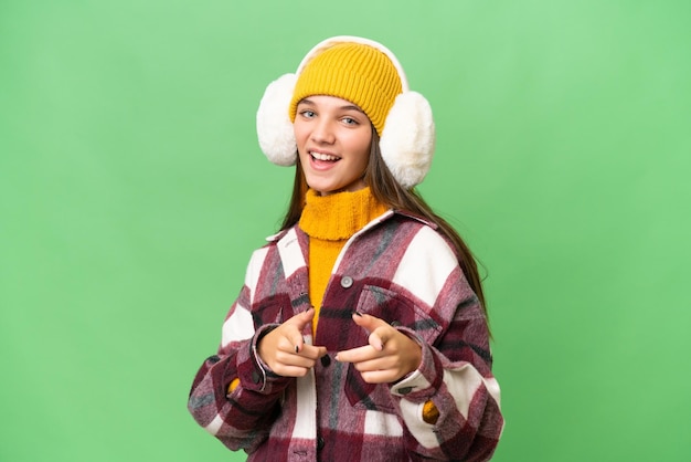 Una adolescente caucásica con manguitos de invierno sobre un fondo aislado apuntando al frente y sonriendo