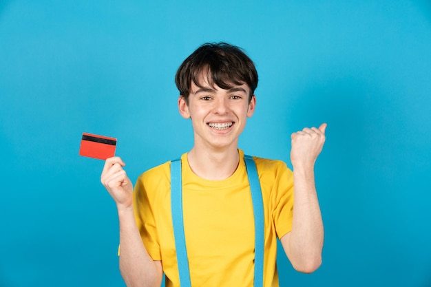 Adolescente celebrando la compra en línea y sosteniendo la tarjeta de crédito con fondo azul