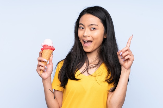 Adolescente chica asiática con un helado de cucurucho en la pared azul apuntando hacia una gran idea