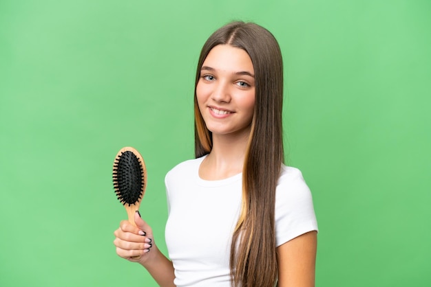 Adolescente chica caucásica con peine sobre fondo aislado sonriendo mucho