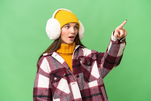 Adolescente chica caucásica vistiendo manguitos de invierno sobre fondo aislado apuntando lejos