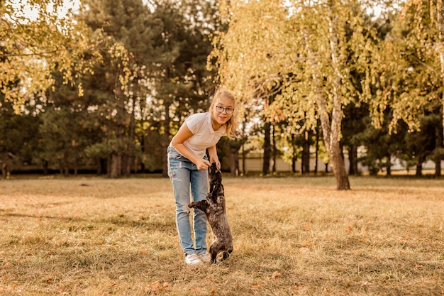 Adolescente chica rubia con gafas grandes riendo y jugando con cachorro spaniel en el cálido parque.