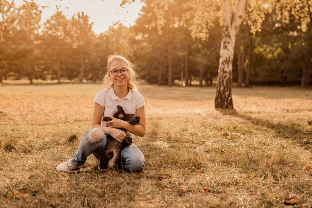 Adolescente chica rubia con grandes gafas riendo y jugando con cachorro spaniel