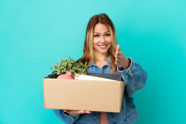 Adolescente chica rubia haciendo un movimiento mientras recoge una caja llena de cosas un apretón de manos para cerrar un buen trato