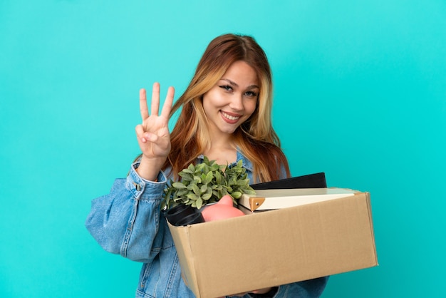 Adolescente chica rubia haciendo un movimiento mientras recoge una caja llena de cosas felices y cuenta tres con los dedos