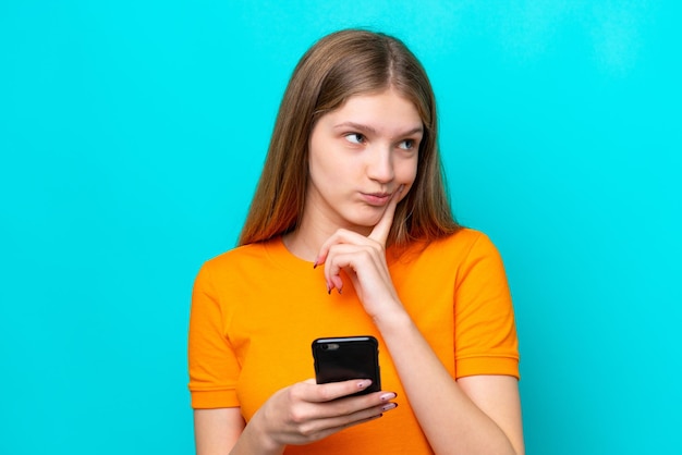 Adolescente chica rusa aislada de fondo azul usando teléfono móvil y pensando