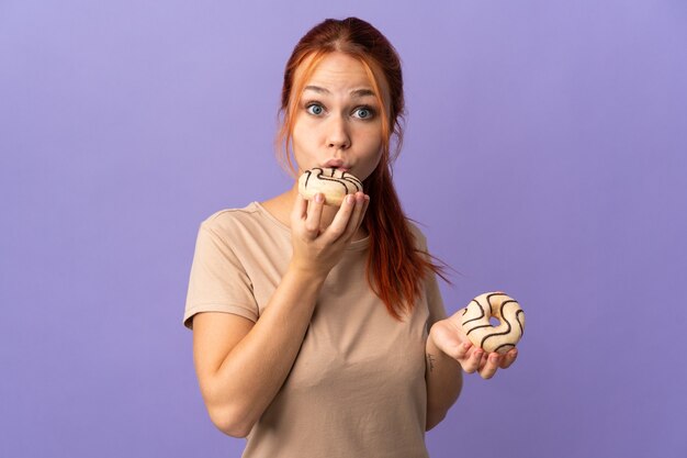 Adolescente chica rusa aislada en la pared púrpura sosteniendo una rosquilla