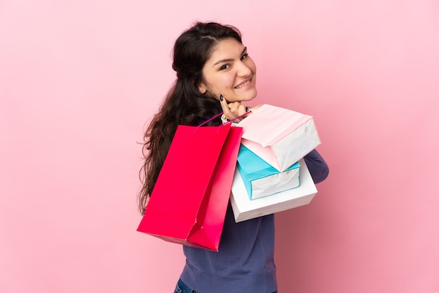 Adolescente chica rusa aislada en la pared rosa sosteniendo bolsas de la compra y sonriendo