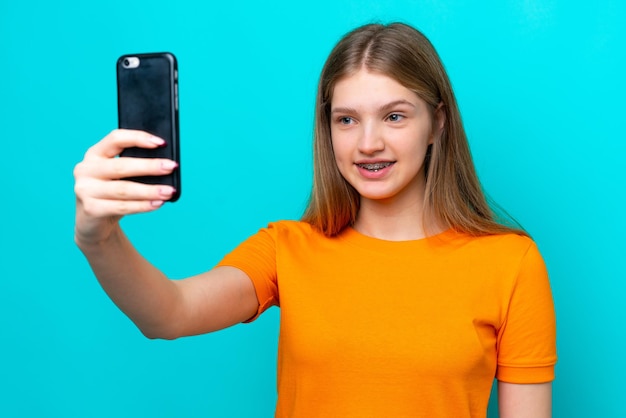 Adolescente chica rusa aislada sobre fondo azul haciendo un selfie con teléfono móvil