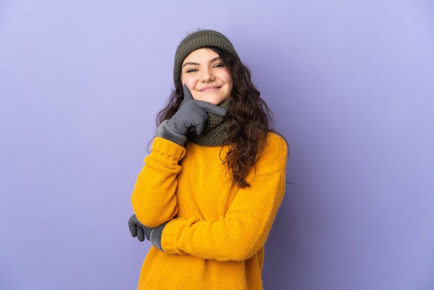 Adolescente chica rusa con sombrero de invierno aislado en la pared púrpura feliz y sonriente