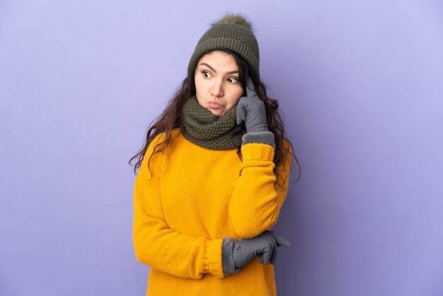 Adolescente chica rusa con sombrero de invierno aislado sobre fondo púrpura pensando en una idea