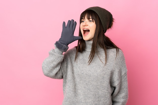 Adolescente chica ucraniana con sombrero de invierno aislado en la pared blanca gritando con la boca abierta