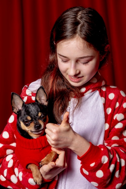 Adolescente y un chihuahua vestidos con un suéter rojo para perros en casa sobre un fondo rojo.