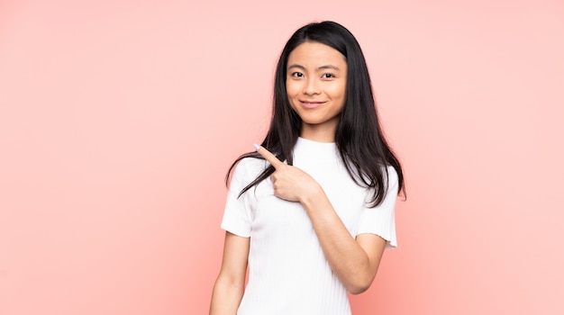 Adolescente China mujer aislada sobre fondo rosa apuntando hacia un lado para presentar un producto