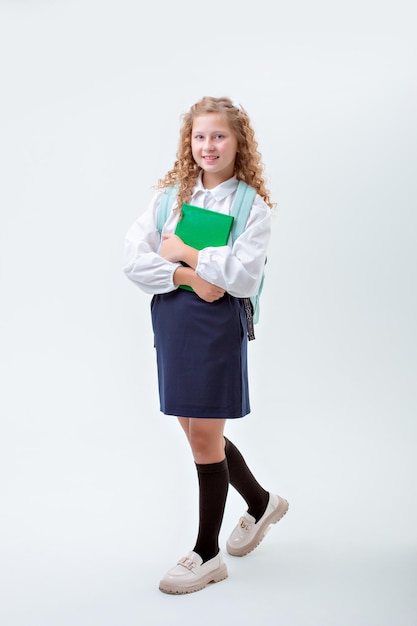 Adolescente colegial em uniforme escolar com uma maleta segurando o livro andando sobre fundo branco