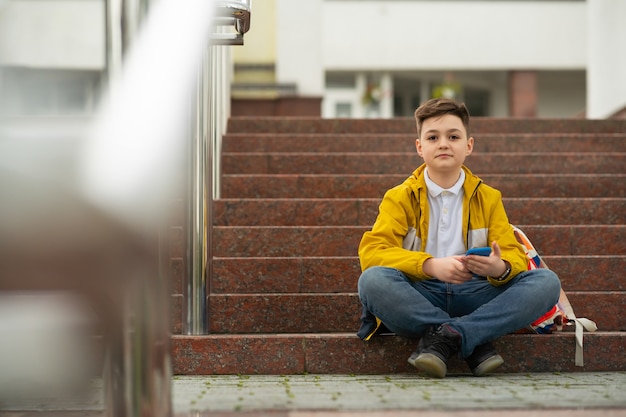 Adolescente colegial se sienta en las escaleras con teléfono