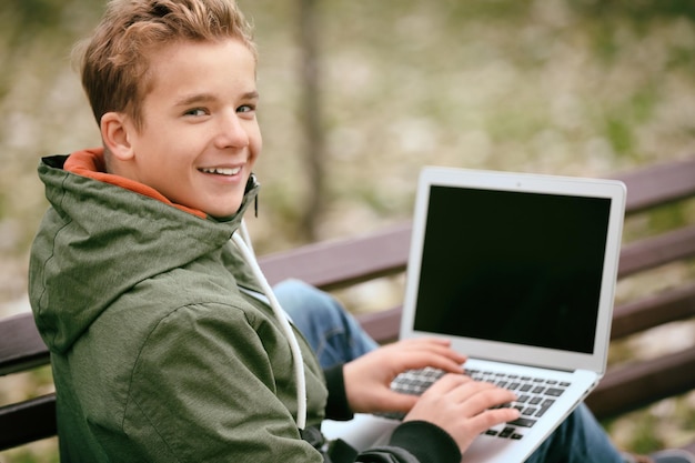 Adolescente com laptop sentado no banco no parque outono