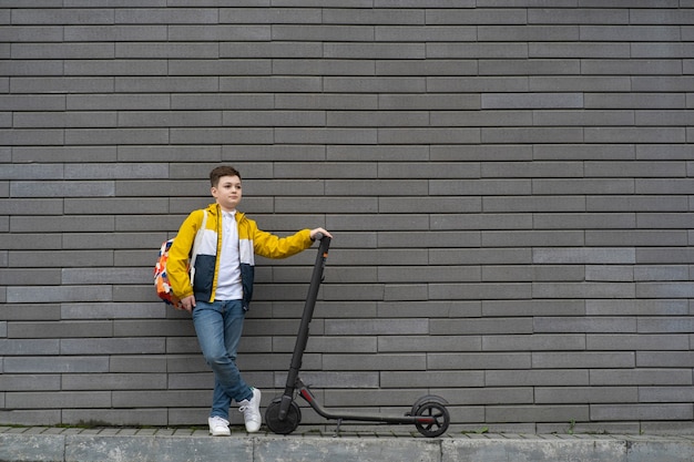 Foto adolescente com mochila e scooter elétrica no fundo da parede de tijolo.