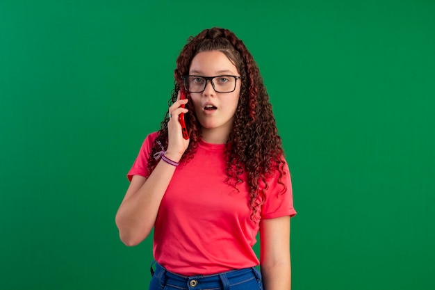 Adolescente com óculos usando celular em poses divertidas em foto de estúdio com fundo verde ideal para corte