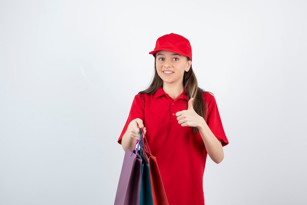 adolescente com uniforme vermelho mostrando o polegar e segurando sacolas de compras