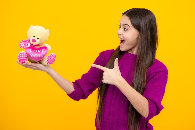 Adolescente com ursinho de pelúcia com coração de amor para o dia dos namorados Menina adolescente segurando um brinquedo de pelúcia isolado em fundo amarelo infância feliz