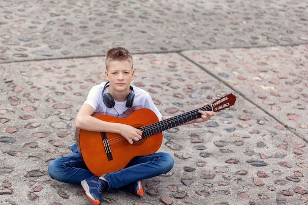 Adolescente com violão e fones de ouvido, sentado no parque.